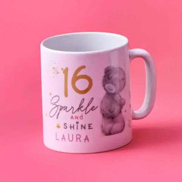 Two personalised mugs on a wooden table, one decorated with festive gingerbread and candy cane designs featuring the name Eloise, accompanied by a small plate of cookies, with a blurred Christmas tree in the background.